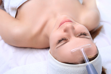 People, beauty, spa, cosmetology and technology concept - close up of beautiful young woman lying with closed eyes having face massage by massager in spa.